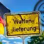 Fotomontage mit einem Schild auf dem „Waffenlieferung“ steht im Vordergrund. Dahinter ist die Deutschlandflagge und ein Fadenkreuz zu sehen | Deutschland liefert wieder vollumfänglich Rüstungsgüter an Israel