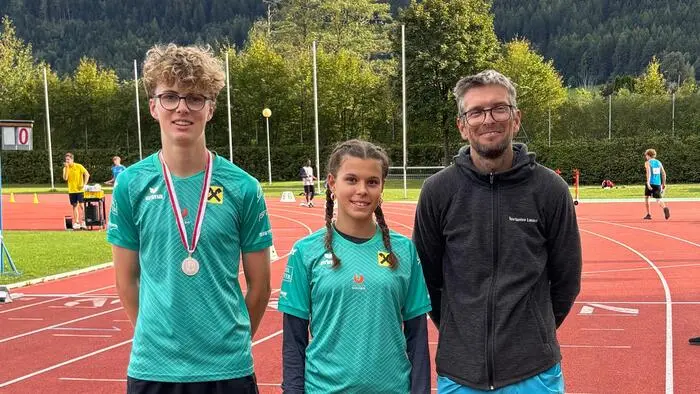 Ein Junge, ein Mädchen und ein Mann auf einer Laufstrecke lachen in die Kamera