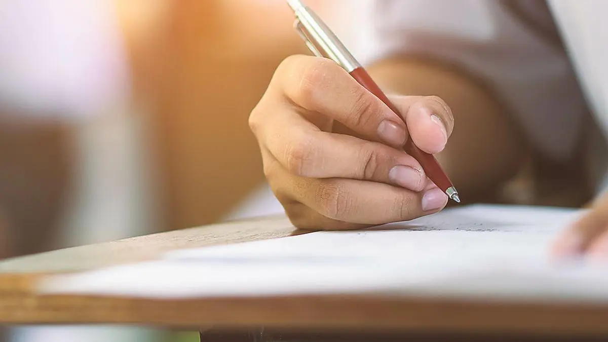 Closeup to hand of student  holding pen and taking exam in classroom with stress for education test .