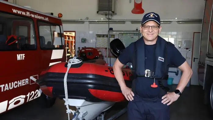 Ein Mann posiert in Feuerwehreinsatzuniform vor einem Einsatzboot für ein Foto.