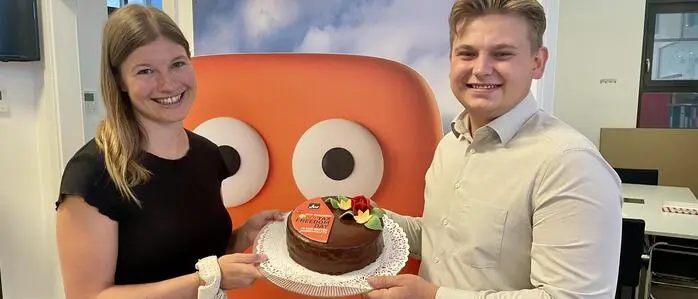Sophie Anderwald und Tobias Vecsei mit einer Torte auf der die orange Fläche für jenen Zeitraum steht, in dem Menschen für die eigene Tasche arbeiten 