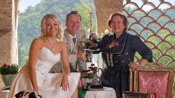Zwei Frauen und ein Mann, elegant für einen Ballabend gekleidet, lächeln in die Kamera.