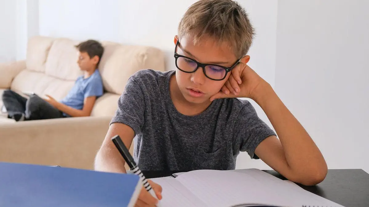 Stay at home, online learning, distance learning, self quarantine concept. Boy start doing homework with books notebooks and other boy using tablet for online lesson