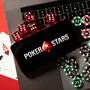 Zu sehen ist eine Fotomontage mit Spielkarten, Jetons und Würfeln auf einer Laptoptastatur, auf der ein Handy mit dem Pokerstars-Logo auf dem Bildschirm liegt | Pokerstars beschäftigt die WKStA
