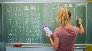 ARCHIV - 17.08.2016, Niedersachsen, Hannover: Eine junge Lehrerin schreibt an eine Schultafel im Mathematikunterricht einer 8. Klasse an einer Integrierten Gesamtschule und blickt dabei auf einen Tablet-Computer. (zu dpa: «Lehrerbildung soll besser auf Schulalltag vorbereiten») Foto: Julian Stratenschulte/dpa +++ dpa-Bildfunk +++