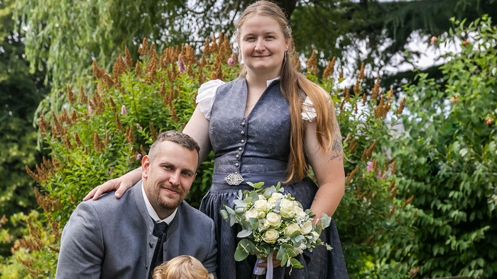 Zu sehen ist ein Brautpaar, das ihre Tochter an den Händen hält