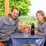 Ein Mann und eine Frau stoßen mit einem Glas Wein an und lächeln in die Kamera.
