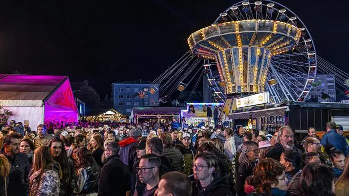 Eine Abendaufnahme vom letztjährigen St. Veiter Wiesenmarkt. Im Vordergrund sind einige Menschen zu sehen, im Hintergrund Fahrgeschäfte.