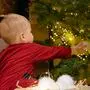 A young mother guides her child as they arrange colorful Christmas balls on a beautifully decorated tree, creating a joyful holiday atmosphere at home.