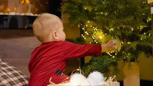 A young mother guides her child as they arrange colorful Christmas balls on a beautifully decorated tree, creating a joyful holiday atmosphere at home.