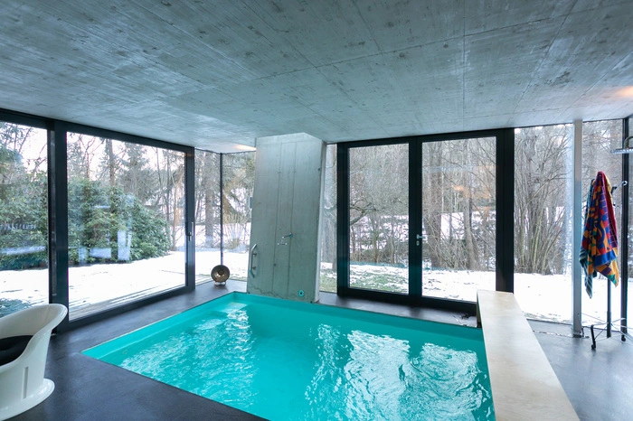 Sichtbeton dominiert im Poolbereich, die breiten Glasfronten lassen sich öffnen und holen die Natur in den Raum.
