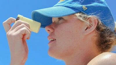 Eine Frau mit blauer Kappe, die sich das Gesicht mit Sonnencreme einschmiert