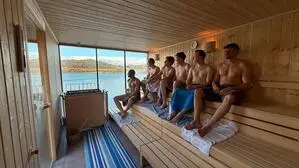 Männer sitzen in einer Holzsauna. Sie sind mit einem Handtuch bedeckt.