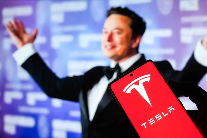 July 4, 2025, Ahmedabad, Gujarat, India: In this photo illustration, the Tesla logo is prominently displayed on a smartphone screen with Mr.Elon Musk in the background. Ahmedabad India - ZUMAs263 20250704_zip_s263_019 Copyright: xSaurabhxSirohiyax