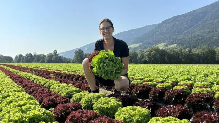 Eine Frau sitzt in einem Feld voller Salat