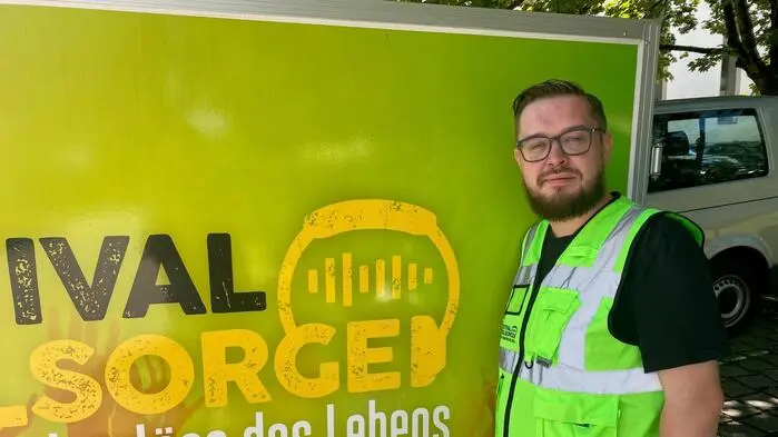 Ein Mann mit gelber Weste steht neben einem Schild der Festival-Seelsorge