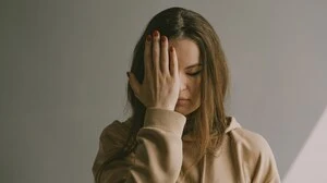 Junge Frau mit Kopfschmerzen, die sich eine Hand vor das Gesicht hält