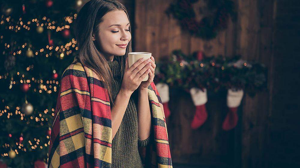 Profile side photo of dreamy positive woman covered checkered blanket feel pleasure on christmas time vacation hold mug smell hot beverage in house with x-mas ornament wreath red socks indoors