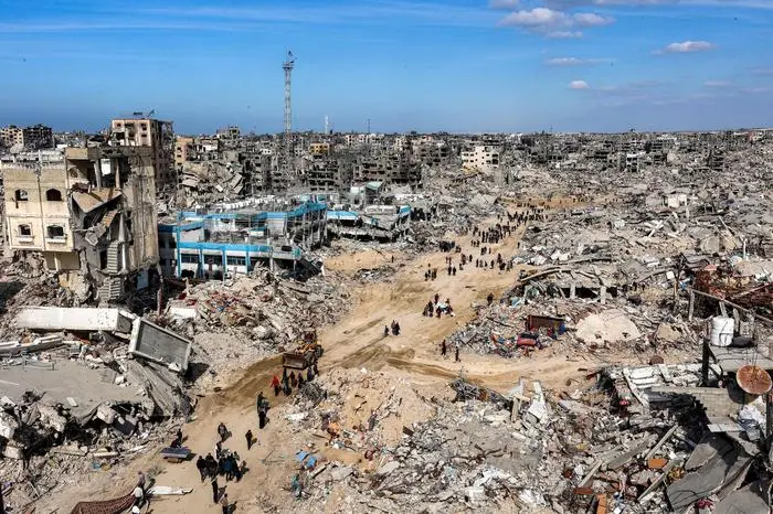 People walk past rubble of collapsed buildings near a destroyed clinic of the United Nations Relief and Works Agency for Palestine Refugees (UNRWA) at the Jabalia camp for Palestinian refugees in the northern Gaza Strip on January 19, 2025 after a ceasefire deal in the war between Israel and Hamas was implemented. The long-awaited ceasefire in the Israel-Hamas war was delayed January 19 after Prime Minister Benjamin Netanyahu said at the last minute that it would not take effect until the Palestinian militant group provided a list of the hostages to be released. (Photo by Omar AL-QATTAA / AFP)