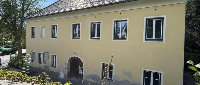 Ein gelbes älsteres Haus mit weißen Fenstern