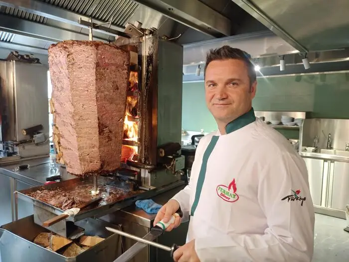 Mit langen, scharfen Messern säbelt Ferhat Yildirim an gigantischen Dönerspießen, dahinter züngeln die Flammen des Holzfeuers hoch.