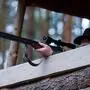 Das Bild zeigt einen Jäger, der von einem hölzernen Hochsitz aus mit einer Jagdwaffe zielt. Die Waffe ist eine doppelläufige Büchse mit Zielfernrohr, und der Jäger hält sie mit ruhiger Hand. Sein Gesicht ist teilweise verdeckt, aber er trägt einen typischen Jagdhut, was ihn als erfahrenen Jäger erkennen lässt. Der Hintergrund zeigt einen dichten Wald mit hohen, geraden Bäumen, die eine ruhige, natürliche Atmosphäre schaffen. Die Szenerie vermittelt den Eindruck einer Jagdsituation in der Dämmerung oder am frühen Morgen, bei der der Jäger geduldig auf Wild wartet. | Der angeklagte Jäger 