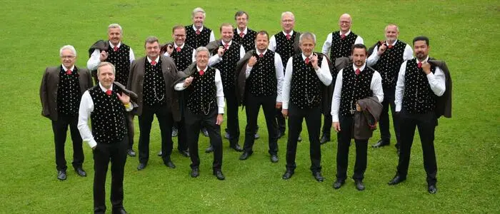 Ein Männerchor in trachtiger Kleidung steht auf einer Wiese.