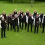Ein Männerchor in trachtiger Kleidung steht auf einer Wiese.