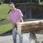 Ein Mann im roten Hemd sägt an einem Baumstamm