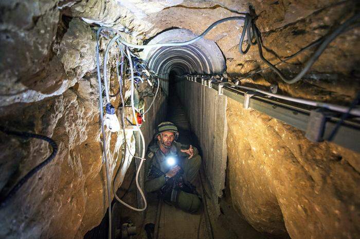 Ein israelischer Soldat leuchtet mit seiner Taschenlampe in einem engen Tunnel in Richtung der Kamera | 2014: Ein israelischer Soldat führt Journalisten durch einen Tunnel, der von militanten Palästinensern genutzt worden sein soll, um über die israelische Grenze zu gelangen 