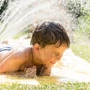 Boy cooling down with garden hose, family in the background on a hot summer day