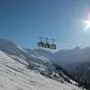 Man sieht Gondeln einen Berg hinauffahren, darunter eine Piste, im Hintergrund blauer Himmel mit Sonne | Auch im Skigebiet Ankogel-Mallnitz kann man noch Ski fahren