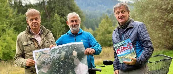 Drei Männer posieren für ein Foto. Zwei halten eine große Karte in der Hand, der andere ein kleines Plakat.