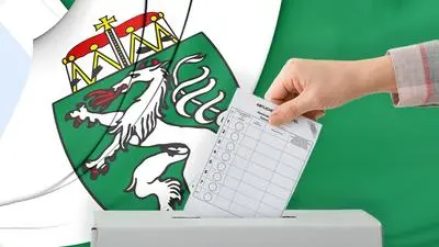 Bild zeigt eine Hand, die einen Stimmzettel in eine Wahlurne wirft. Im Hintergrund ist eine Flagge mit Farben und Wappen der Steiermark zu sehen. | Die Steiermark hat gewählt: Das sind die Ergebnisse der Gemeinderatswahlen 2025