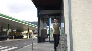 Eine Frau steht auf einer Treppe vor einem Geschäft neben der Straße, im Hintergrund sieht man eine Tankstelle