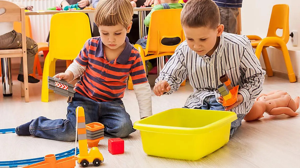 Two cute little boys playing with toy railway in kindergarten