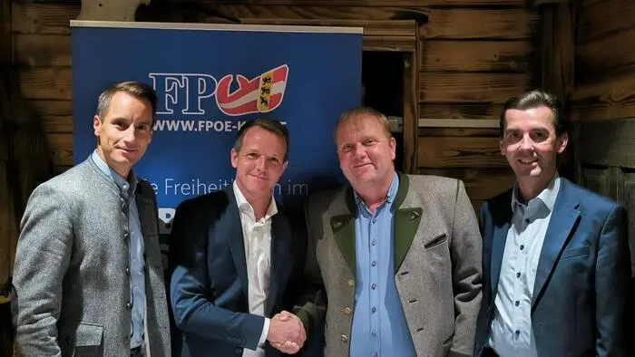 Vier männliche Politiker lachen in die Kamera. Die zwei in der Mitte schütteln die Hände.