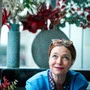 Eine Frau sitzt vor einem Blumenschmuck und lächelt