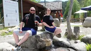 Ein Mann und eine Frau sitzen vor einer Gaststätte auf einem Felsen und lächeln in die Kamera. Der Mann hält ein Glas Bier in Händen, die Frau ein Eis.