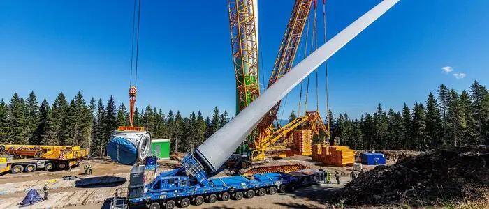 Ein Kran hebt den Rotor eines Windrads an, daneben sieht man den Turm der Anlage