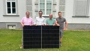 Vier Männer stehen vor einem historischen Gebäude und halten ein PV-Paneel fest
