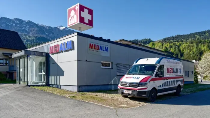 Die Arztpraxis „MedAlm“ mit Rettungsauto davor 