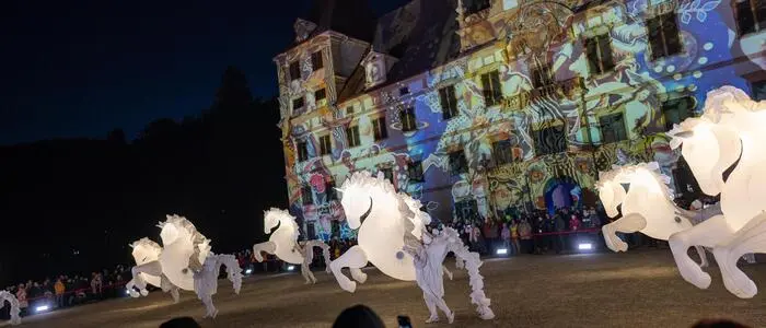 Lichter werden auf eine Schlossfassade projiziert. Im Vordergrund sind leuchtende Pferde aus Kunststoff zu sehen.