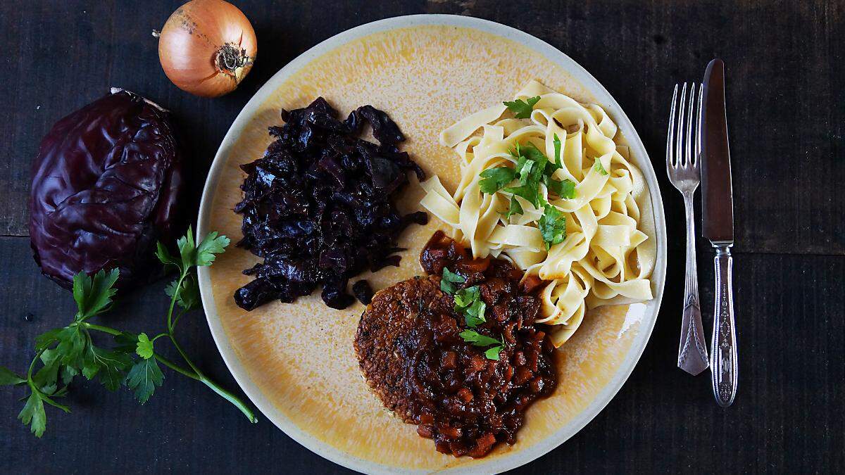 Ein luftiges Tagliatelle-Knuel bildet mit weihnachtlichem Rotkraut und der krossen Veggie-Frikadelle ein Trio auf dem Teller