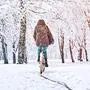Woman rides a bicycle in a snowfall in a park. Seasonal weather concept