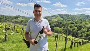 Auf dem Foto sieht man einen jungen Mann, der in einem Weingarten steht und eine Weinflasche in den Händen hält | Winzer Johannes Pichler (27) im Weingarten des besten Sauvignon Blancs Österreichs