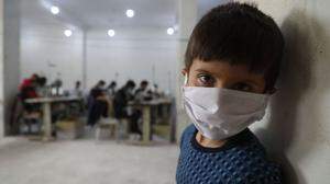 Erst der Krieg, dann Corona: ein Bub in der umkämpften nordsyrischen Stadt Idlib. Im Hintergrund werden Atemschutzmasken genäht 