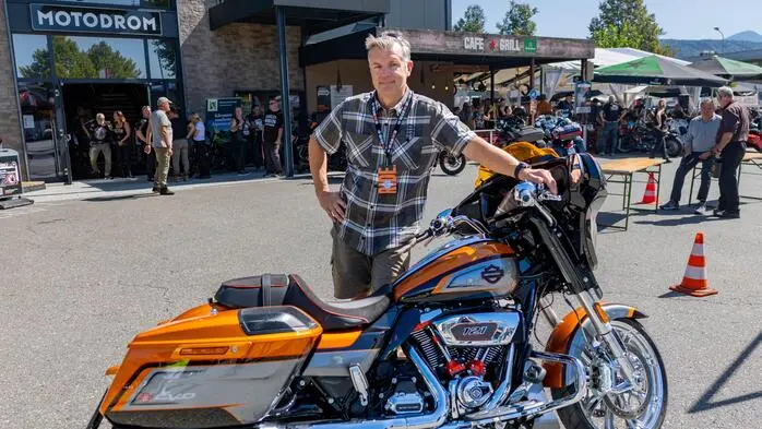 Ein Mann in Karohemd lehnt sich an eine Harley Davidson