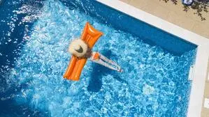 Luftaufnahme einer Frau auf einer Luftmatratze im Swimmingpool | Aus der Luft ermitteln Wasserversorger die Größe von privaten Pools