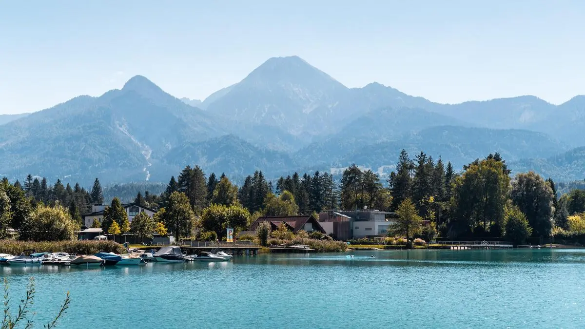 Blick auf einen türkisblauen See, dahinter Bäume und Berge am Horizont
